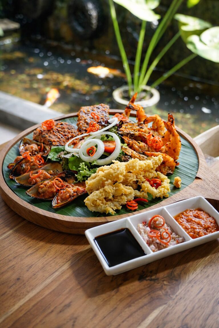 The seafood platter photographed beside the koi pond, with a three-compartment dish of sambals in the foreground.