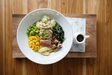 Overhead view of a tuna poke bowl on a teak board with a jug of soy ginger dressing.