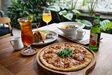 A thin crust pizza topped with tuna, mozzarella, arugula and raw shallot sambal matah, with iced tea alongside.
